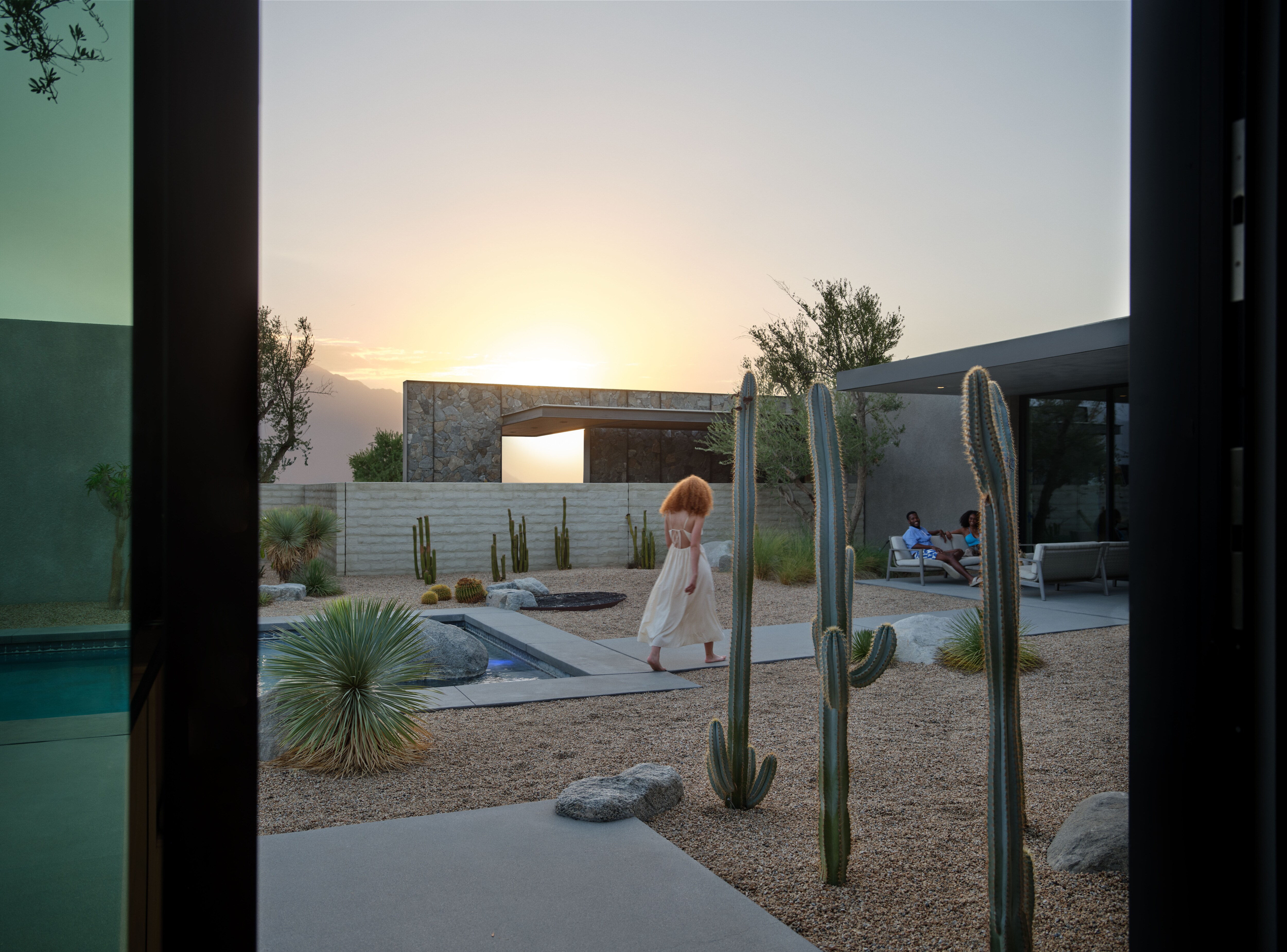 A woman walks past two cacti to join her friends in the backyard of a desert vacation rental.